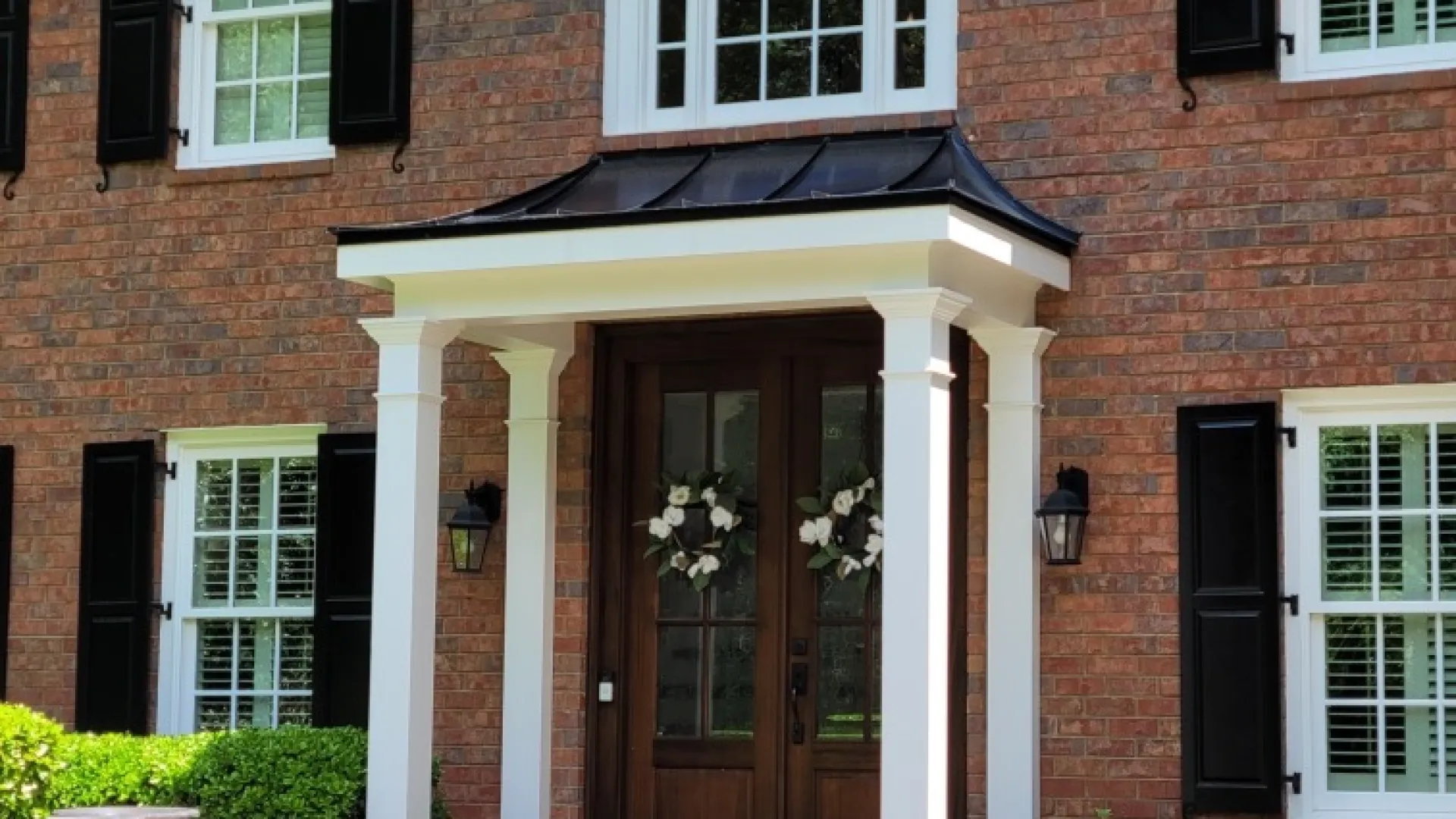 Charming brick house with a welcoming entryway and elegant porch design surrounded by lush greenery.