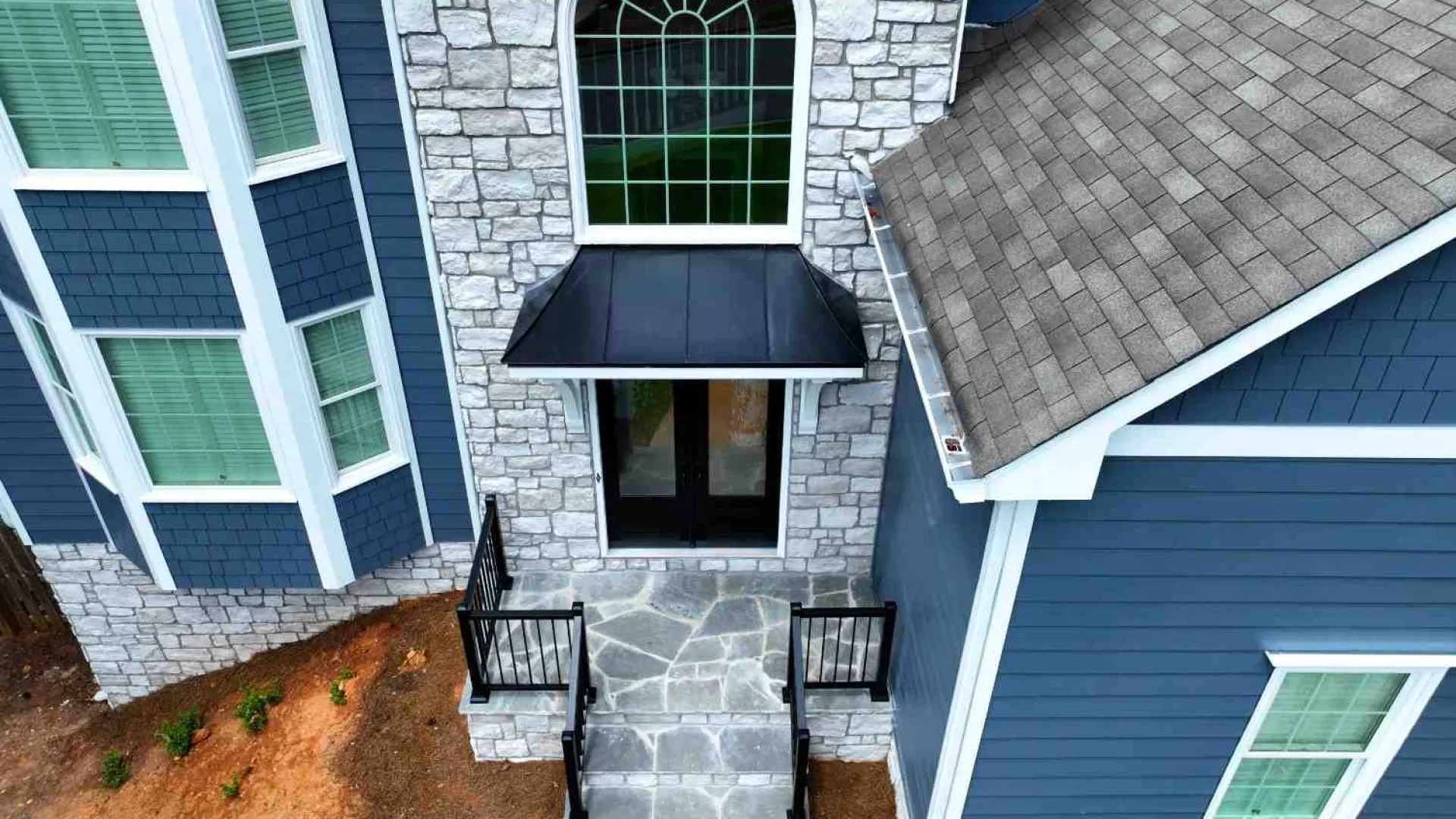 Front entrance of a blue house with stone facade, large arched window, and black metal awning above door.