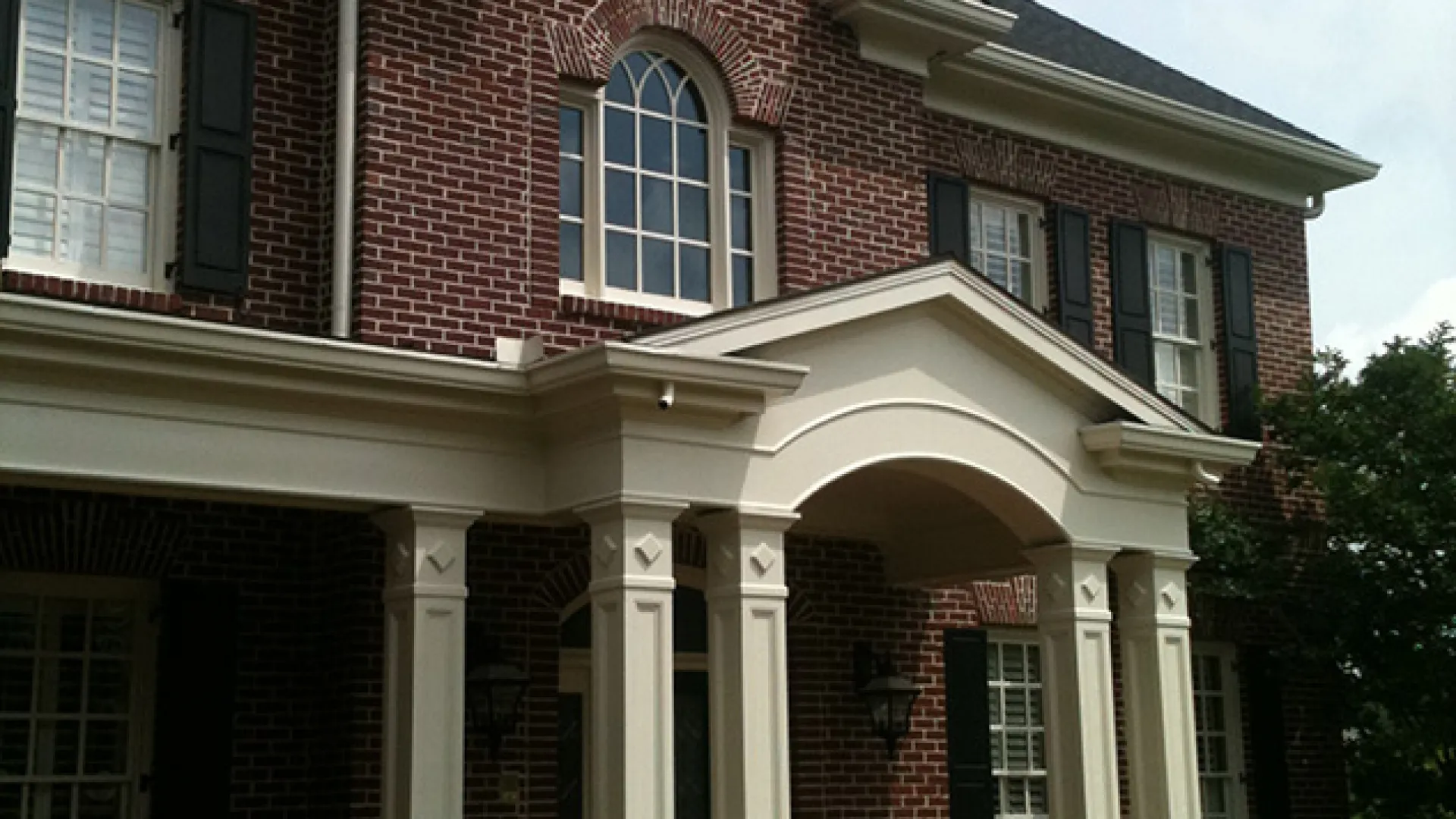 Elegant brick house with a white portico and classic windows, surrounded by lush greenery.