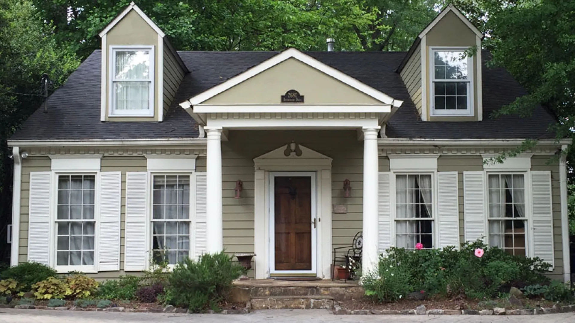 Charming two-story home with a gabled roof, front porch, and lush greenery in the yard.
