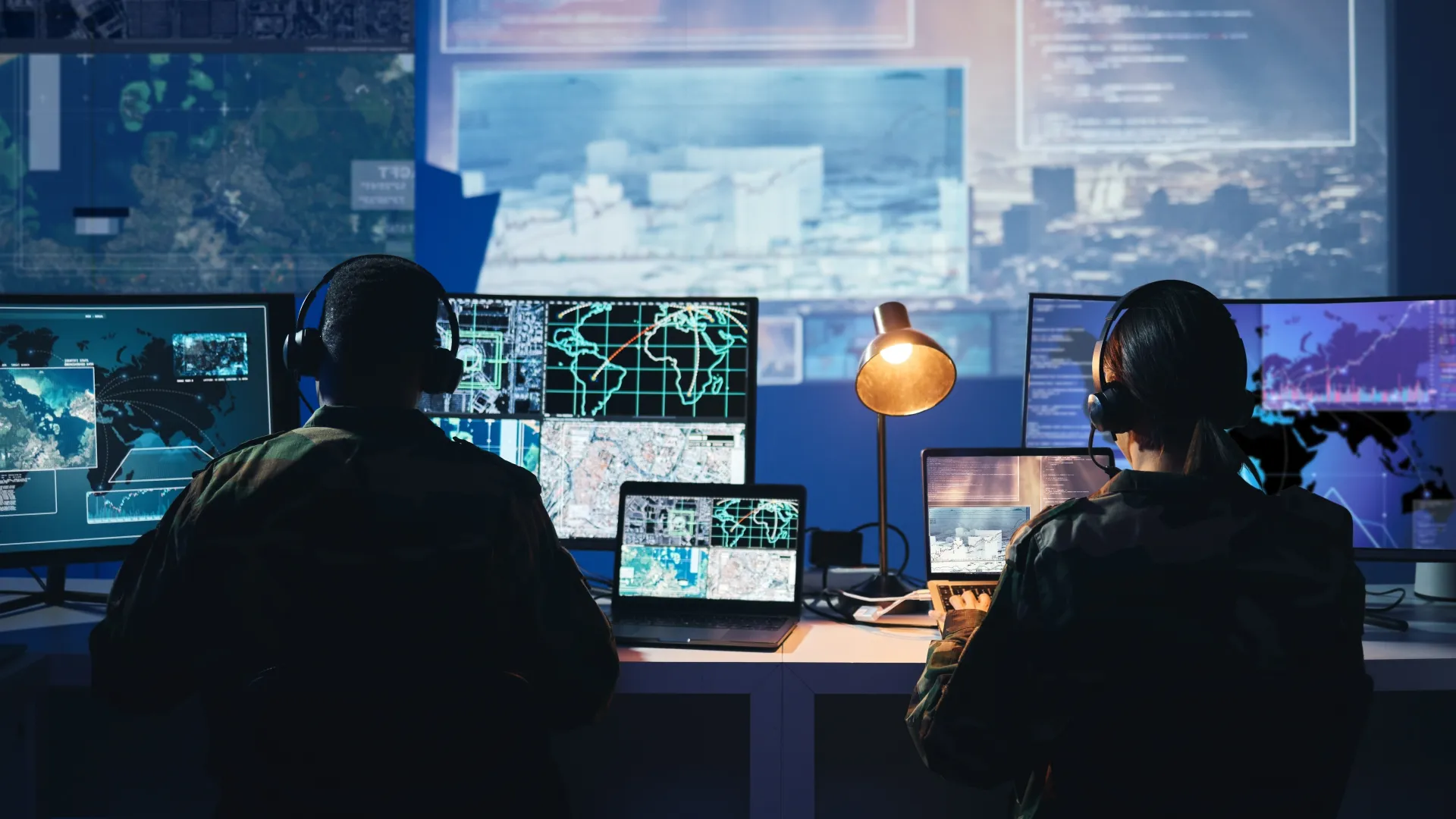 Military personnel monitor multiple screens with maps and data in a tactical setting.