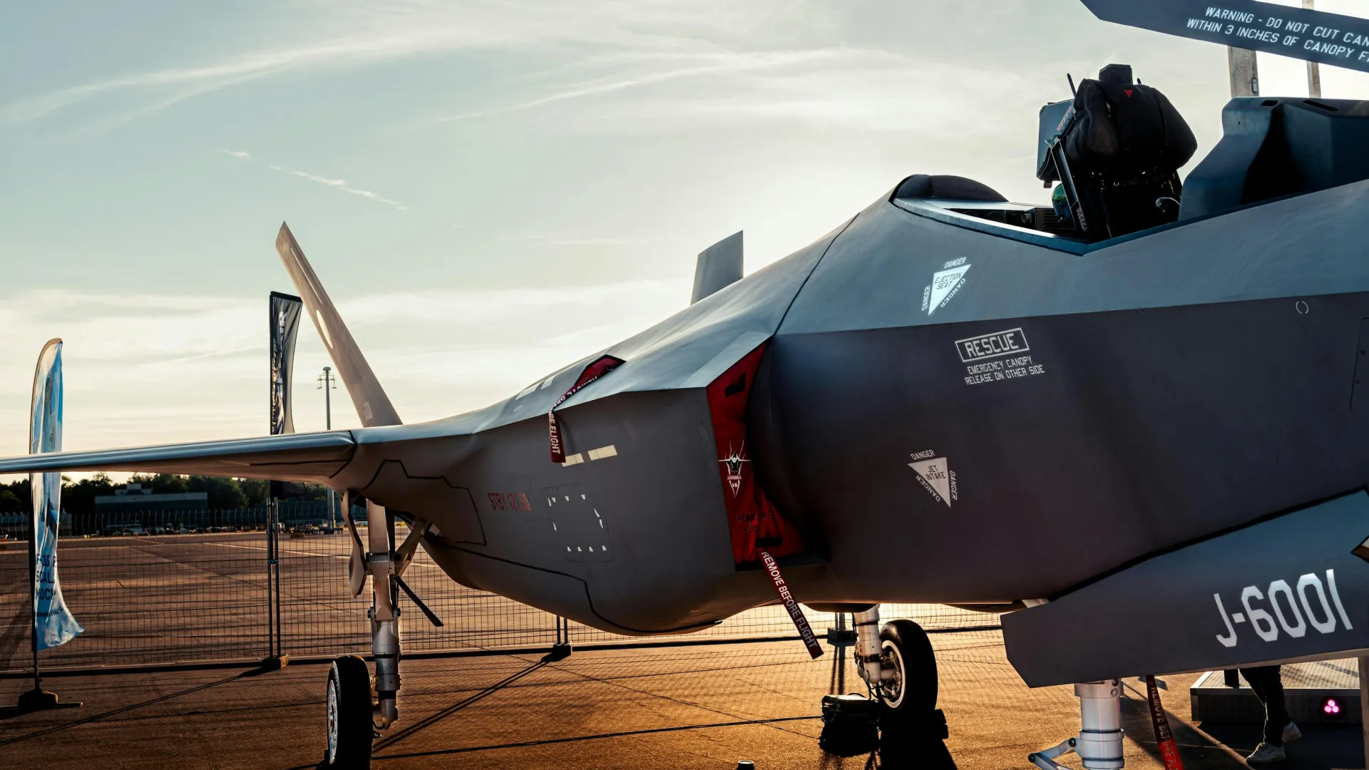 Military stealth fighter jet parked on runway at sunset with detailed fuselage and cockpit view