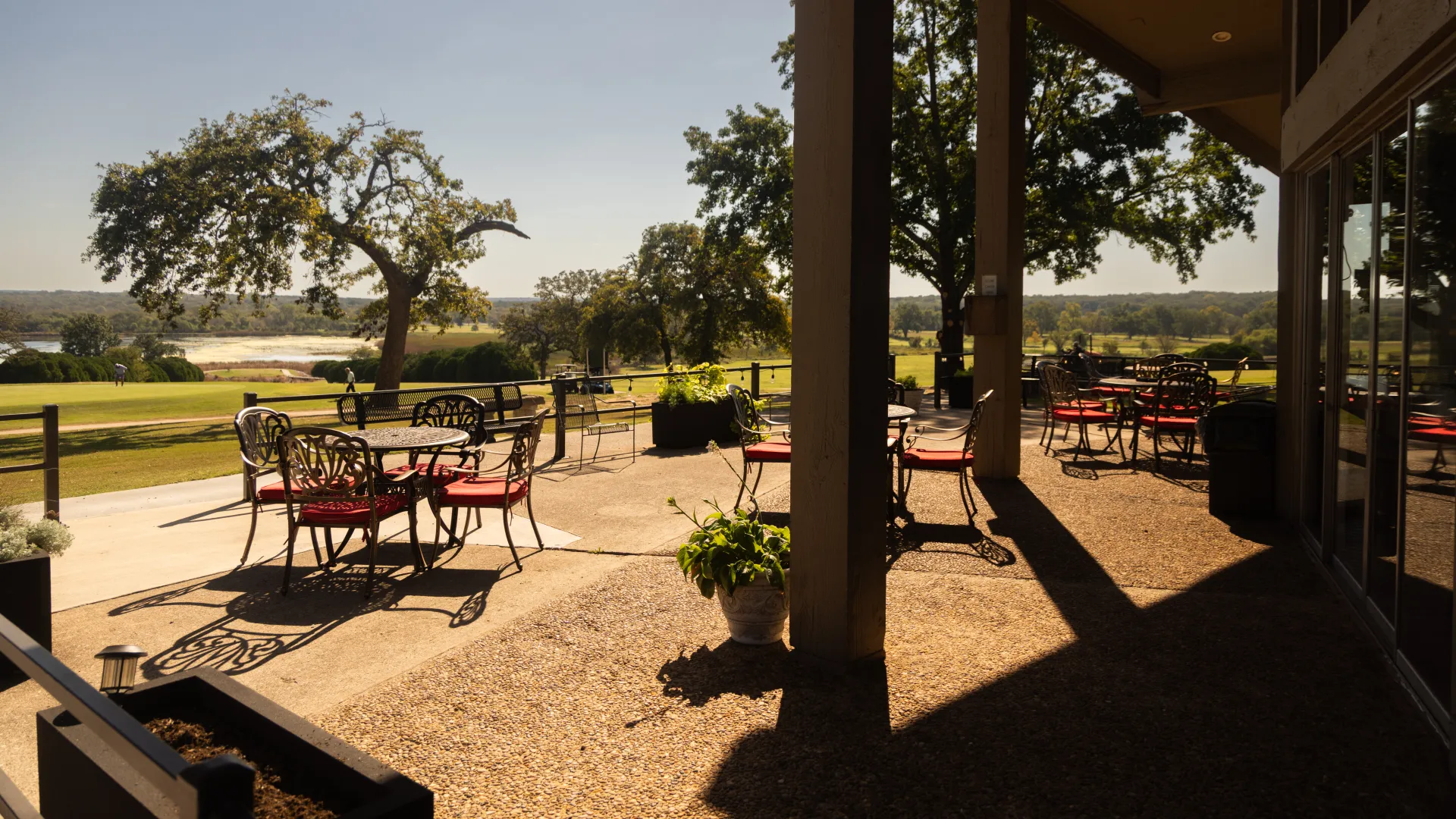 Outdoor patio with wrought iron tables and red chairs overlooking green landscape and trees on a sunny day