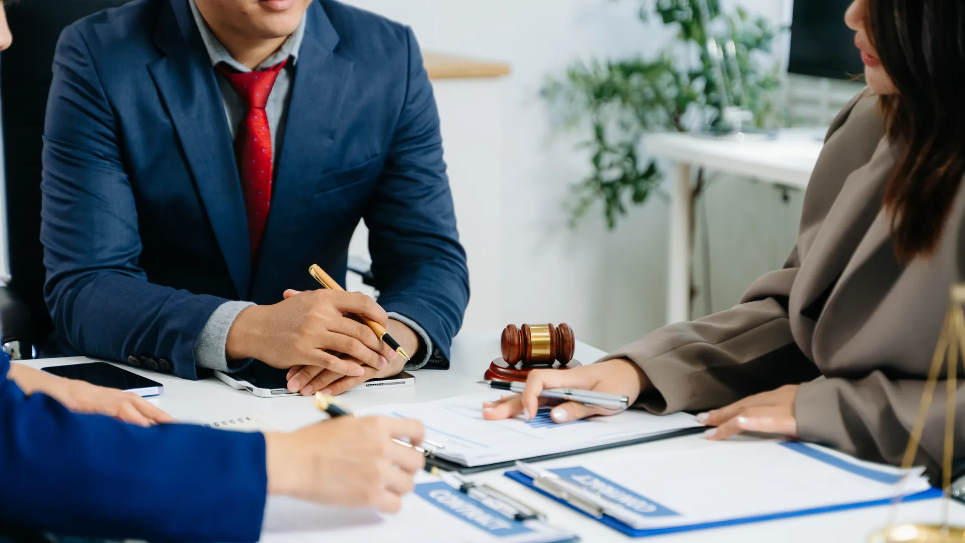Professionals in formal attire discussing documents with a gavel and clipboard on the table in a law office.