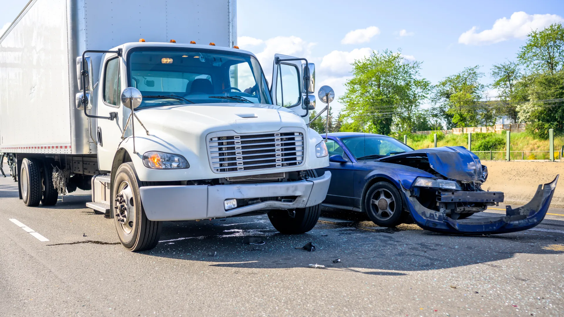 White box truck and blue sedan with front-end damage after a collision on a sunny highway.