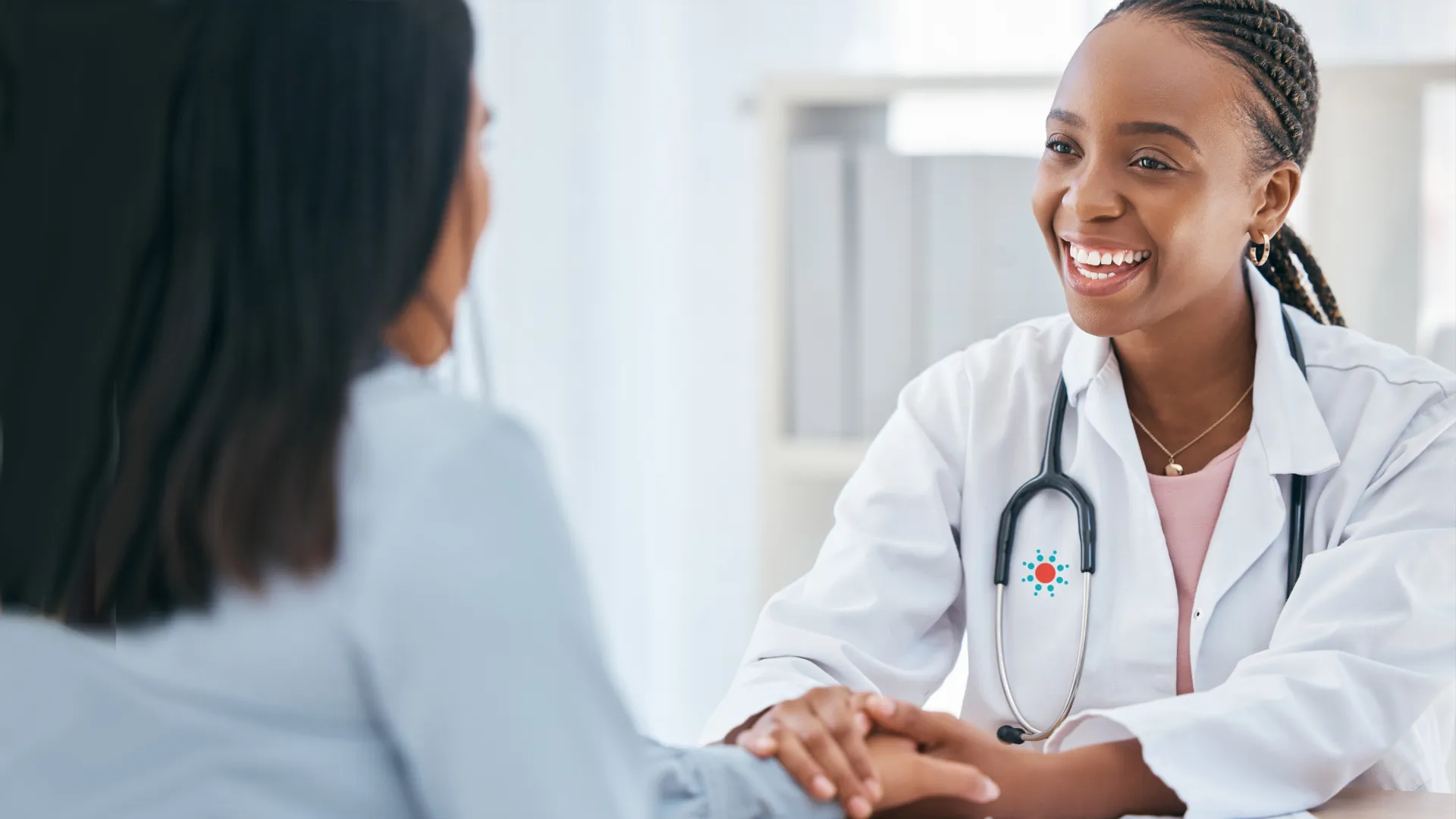 A smiling doctor in a white coat consulting with a patient in a bright office setting.