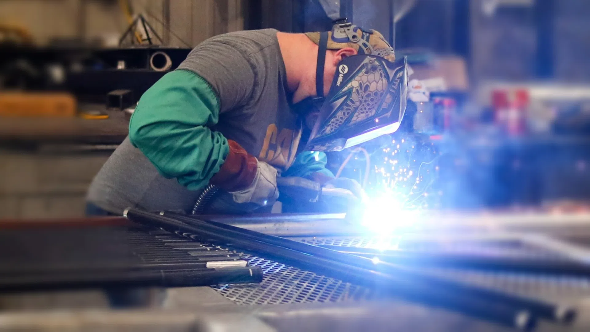 Welder wearing protective gear sparks metal welding in workshop with tools and equipment in background.