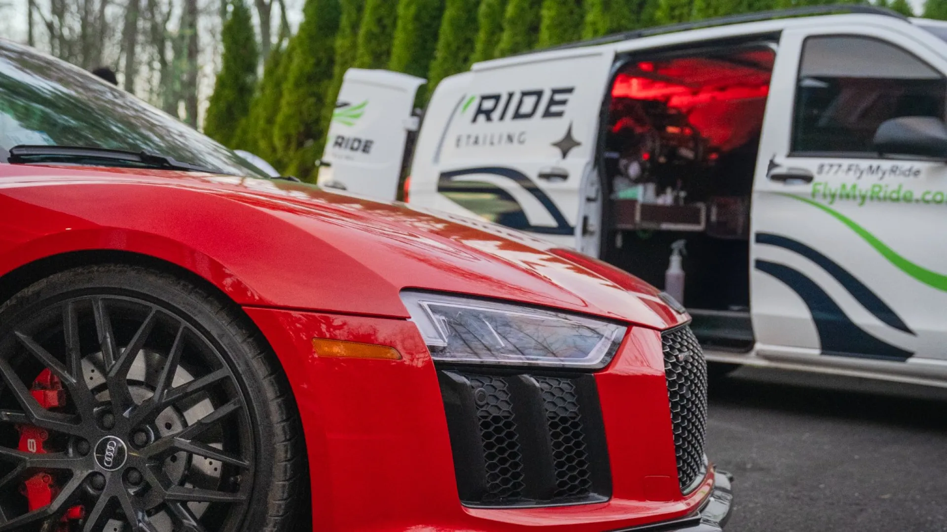 Close-up of a red Audi sports car with a Ride Detailing van in the background on a paved surface.