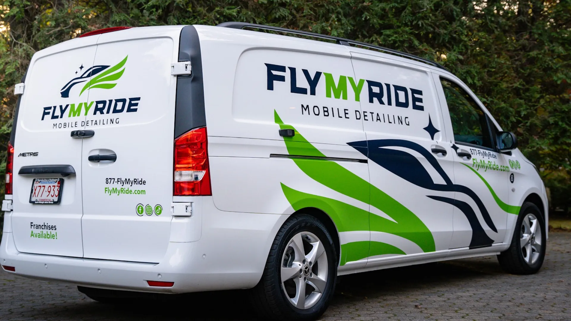 Fly My Ride mobile detailing van parked amidst greenery, featuring eye-catching graphics and branding.