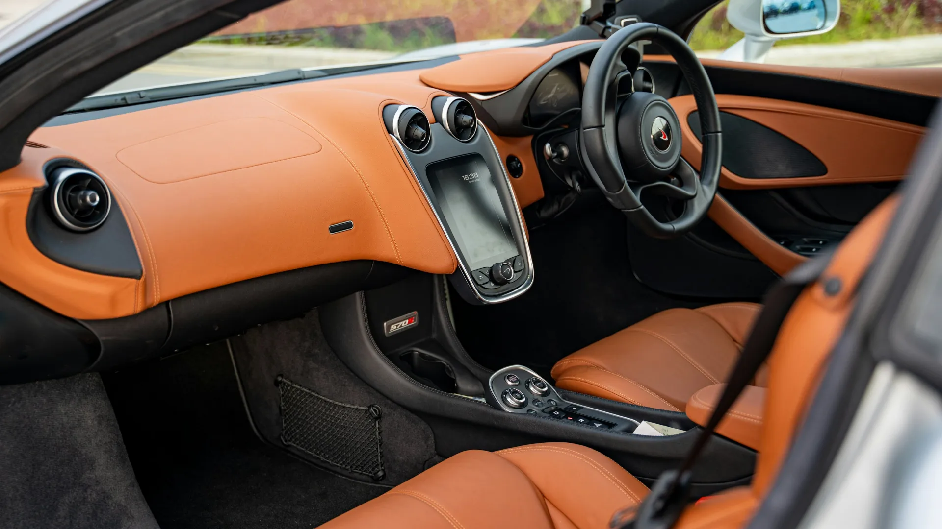 Luxury car interior with tan leather seats, touchscreen display, and modern dashboard design under natural light.