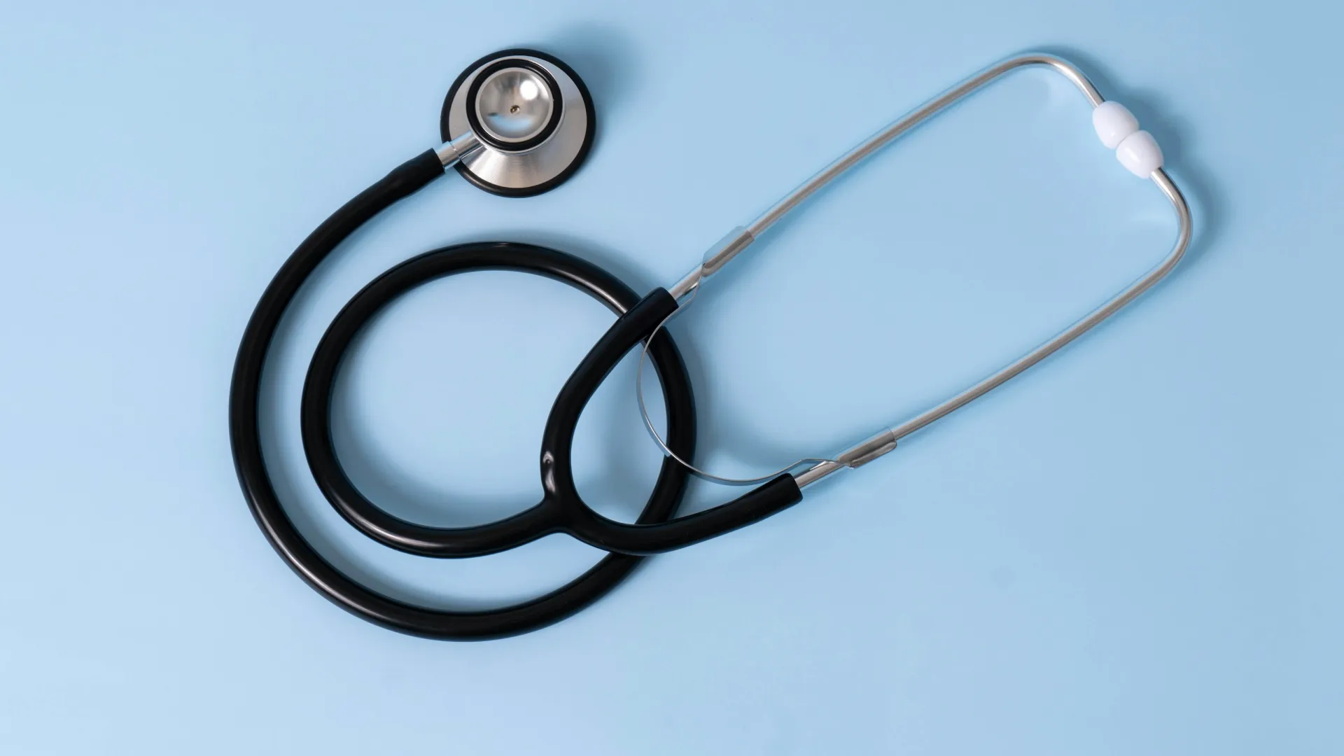 Black and silver stethoscope on a light blue background, symbolizing medical examination and healthcare.