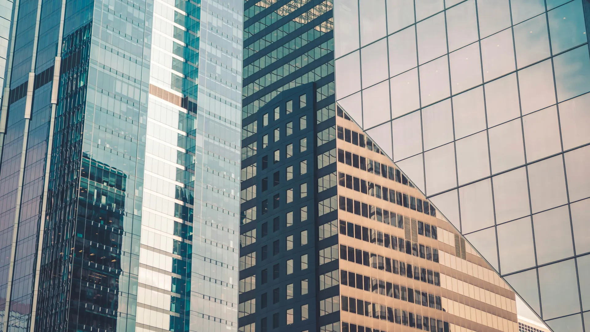 Modern glass skyscrapers reflecting each other under soft light in an urban cityscape.