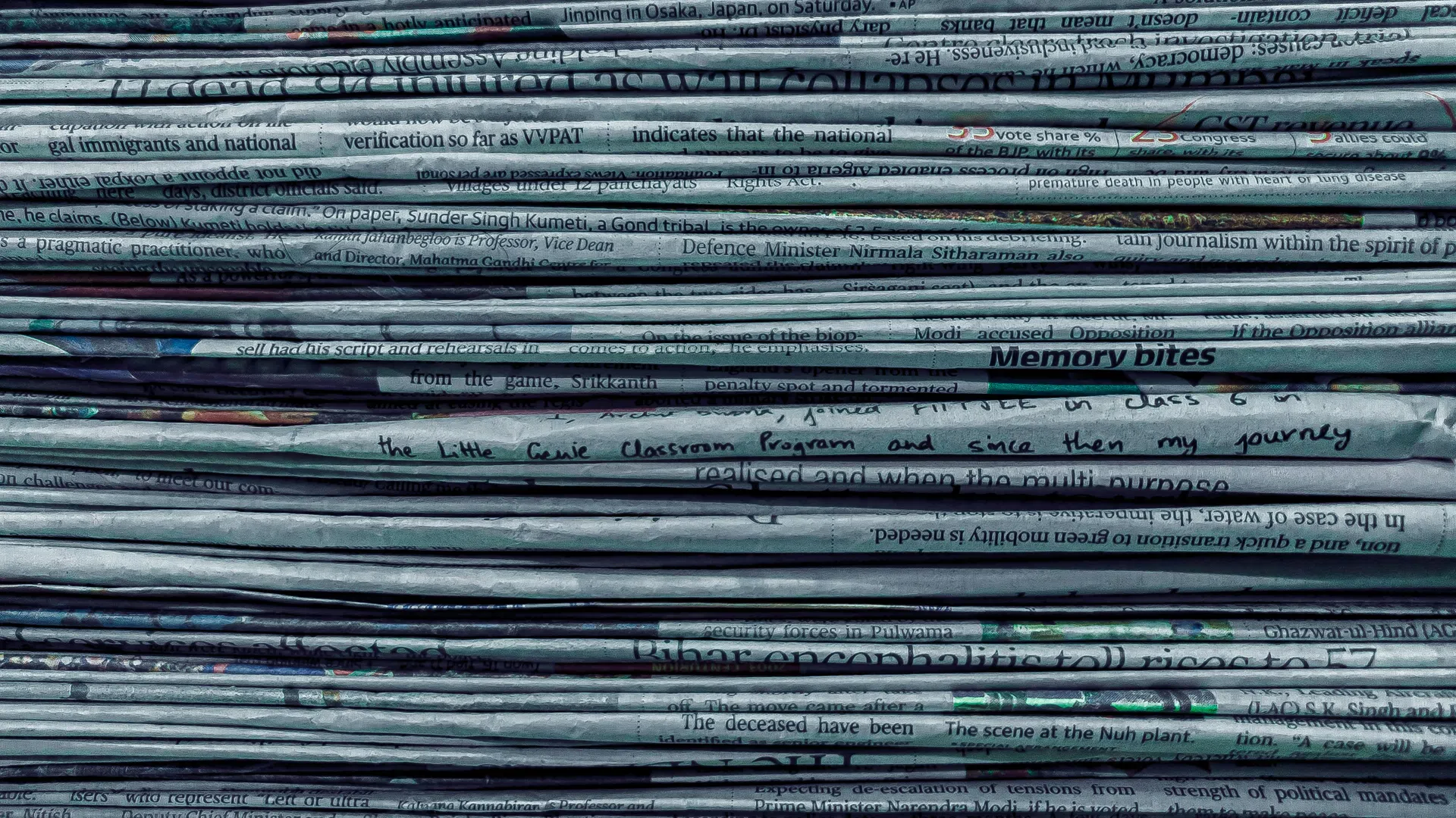 Stacked newspapers showing folded pages with visible black and white text lines and headlines
