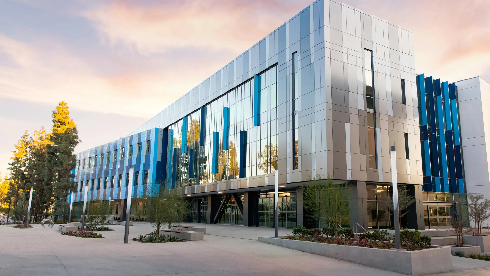 Modern office building with reflective glass windows and blue vertical accents under a colorful sunset sky.