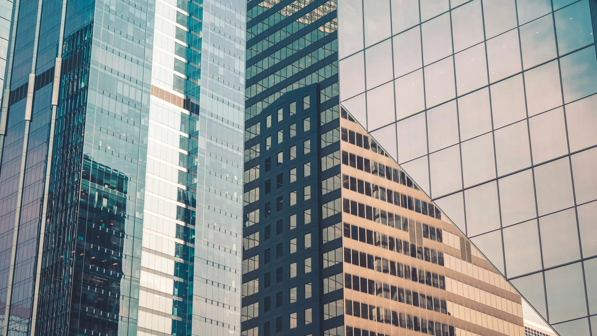 Modern glass skyscrapers reflecting light and surrounding buildings in an urban cityscape.