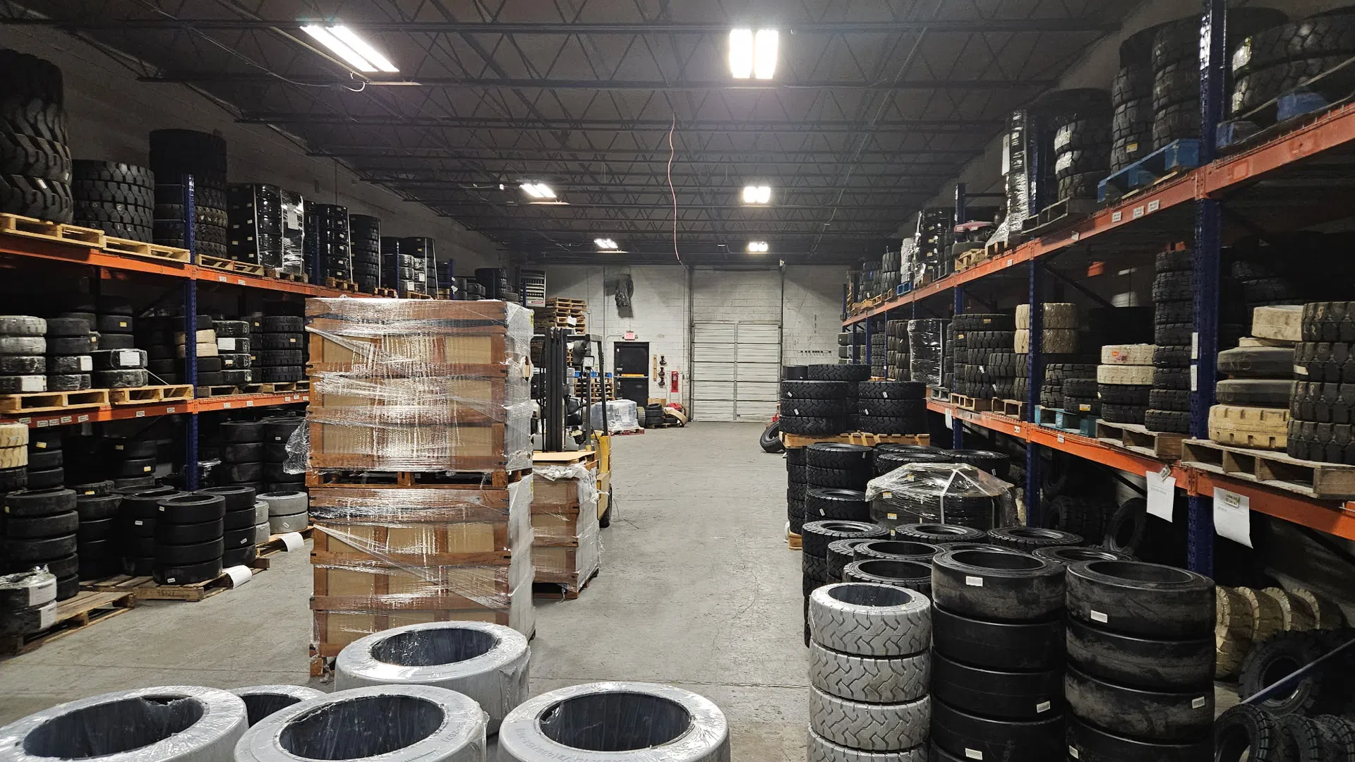 Warehouse interior filled with stacks of various tires on shelves and pallets under bright overhead lights.