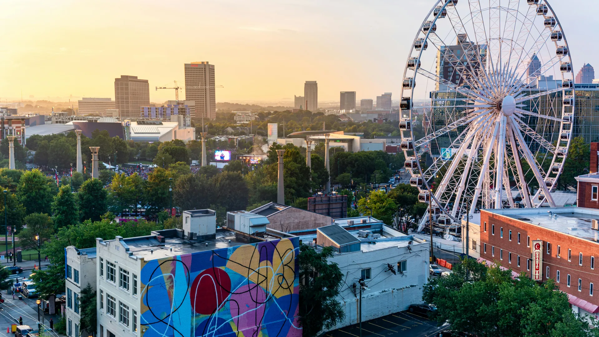 Sunset cityscape featuring a colorful mural, large Ferris wheel, and downtown skyline in the background.