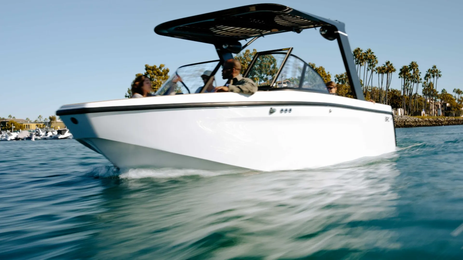 White motorboat cruising on calm water near palm trees under clear blue sky with passengers on board.