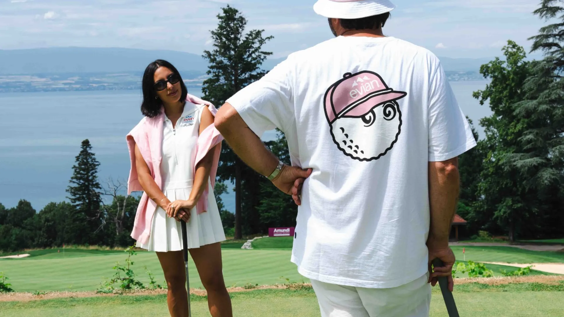 Man and woman playing golf on a green course with lake and trees in the background on a sunny day