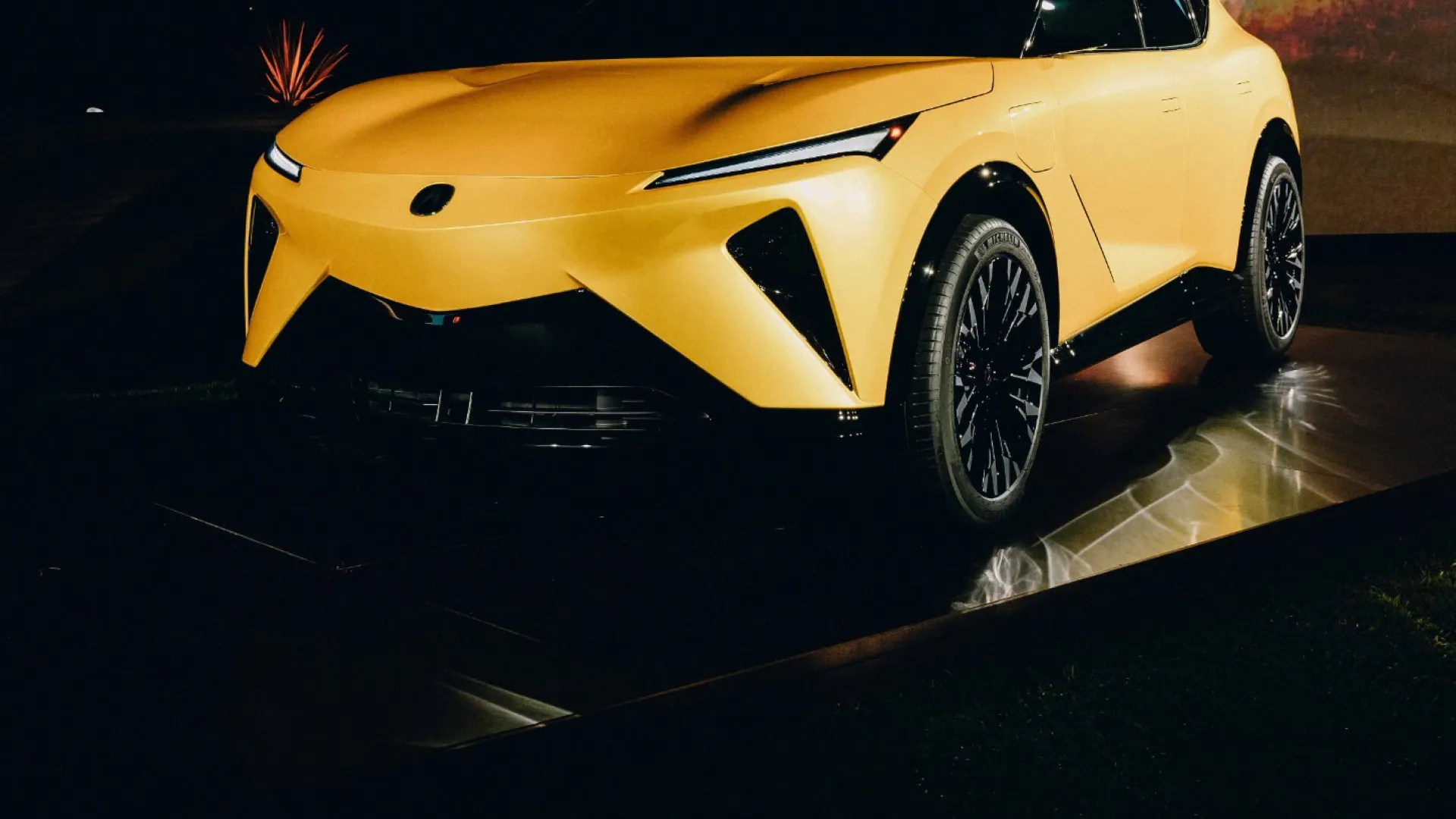 Sleek yellow modern electric SUV showcased under dim lighting with sharp angular design and black wheels.