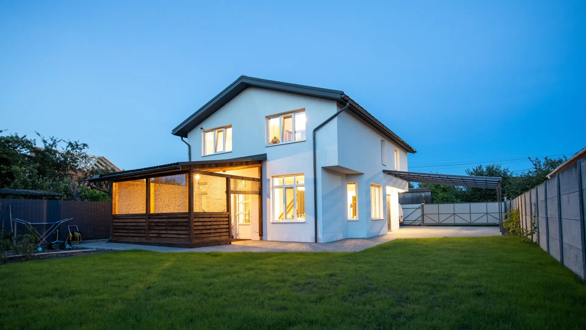 Modern two-story house with illuminated windows and a garden at dusk.