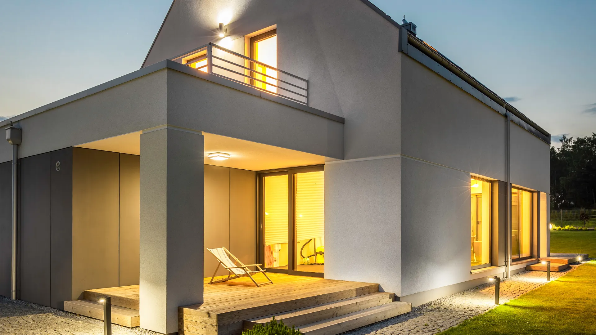 Modern house exterior with illuminated windows and outdoor seating at dusk.