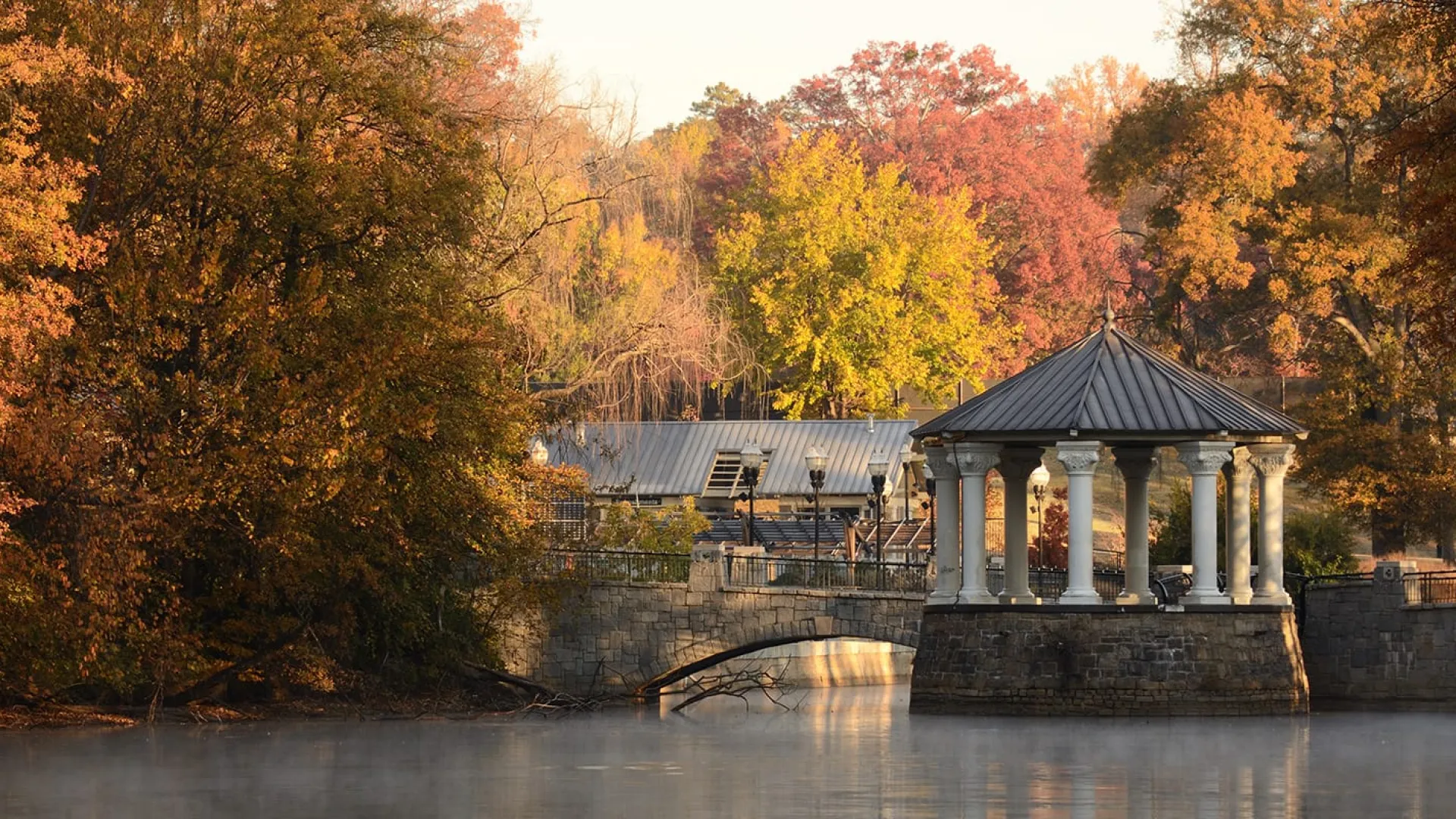 a building with pillars and a bridge over water with trees in the background