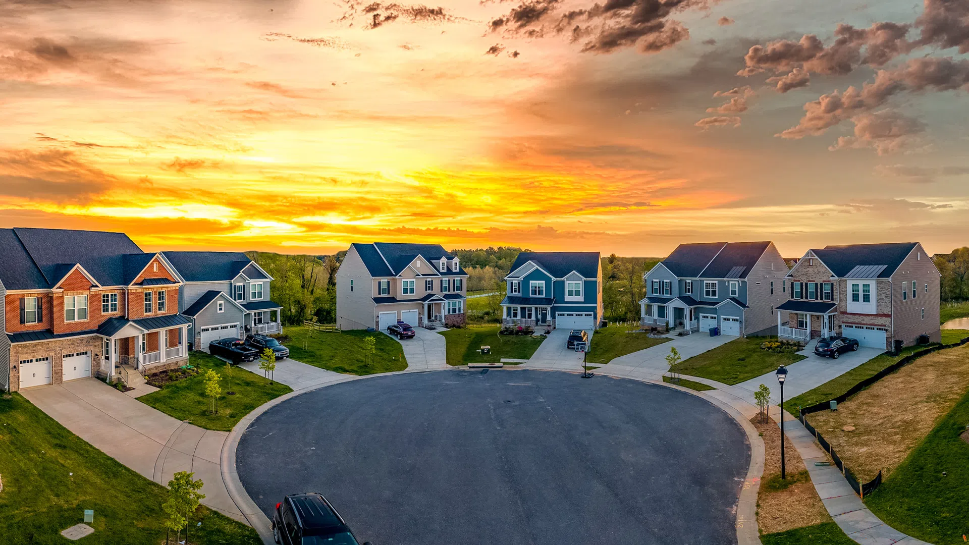 Sunset over a suburban cul-de-sac with modern two-story houses and manicured lawns.