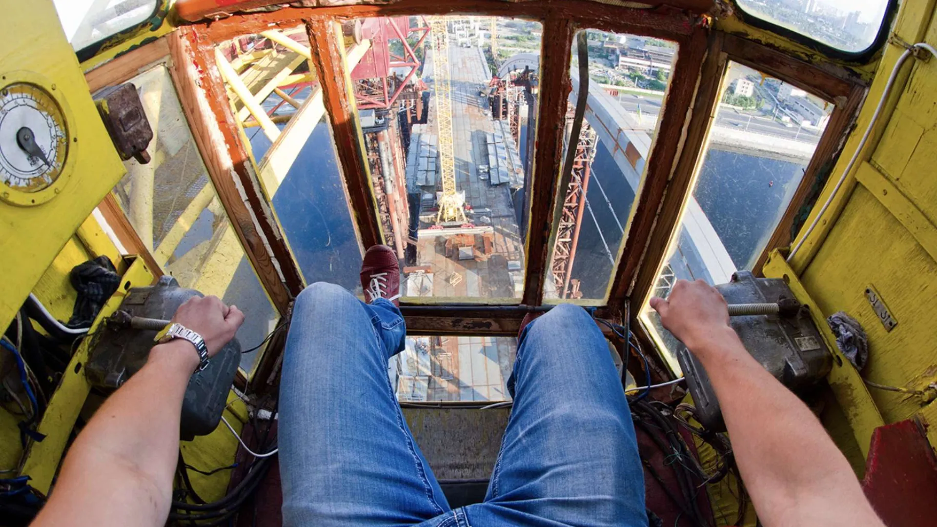 Two construction workers wearing orange helmets installing large glass panels on a building facade.