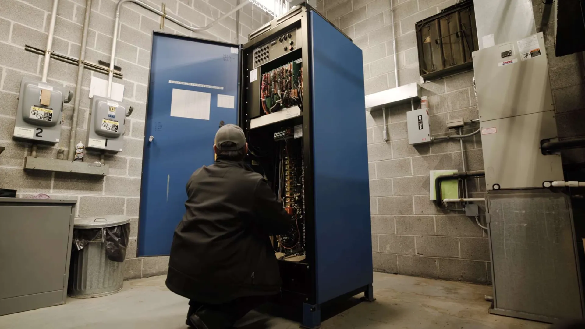 Electrician wearing yellow helmet fixing colorful wires in electrical control panel with circuit breakers.