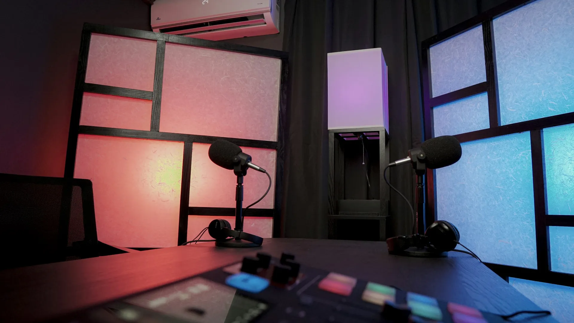 Podcast studio setup with microphones, headphones, sound mixer, and colorful illuminated acoustic panels.