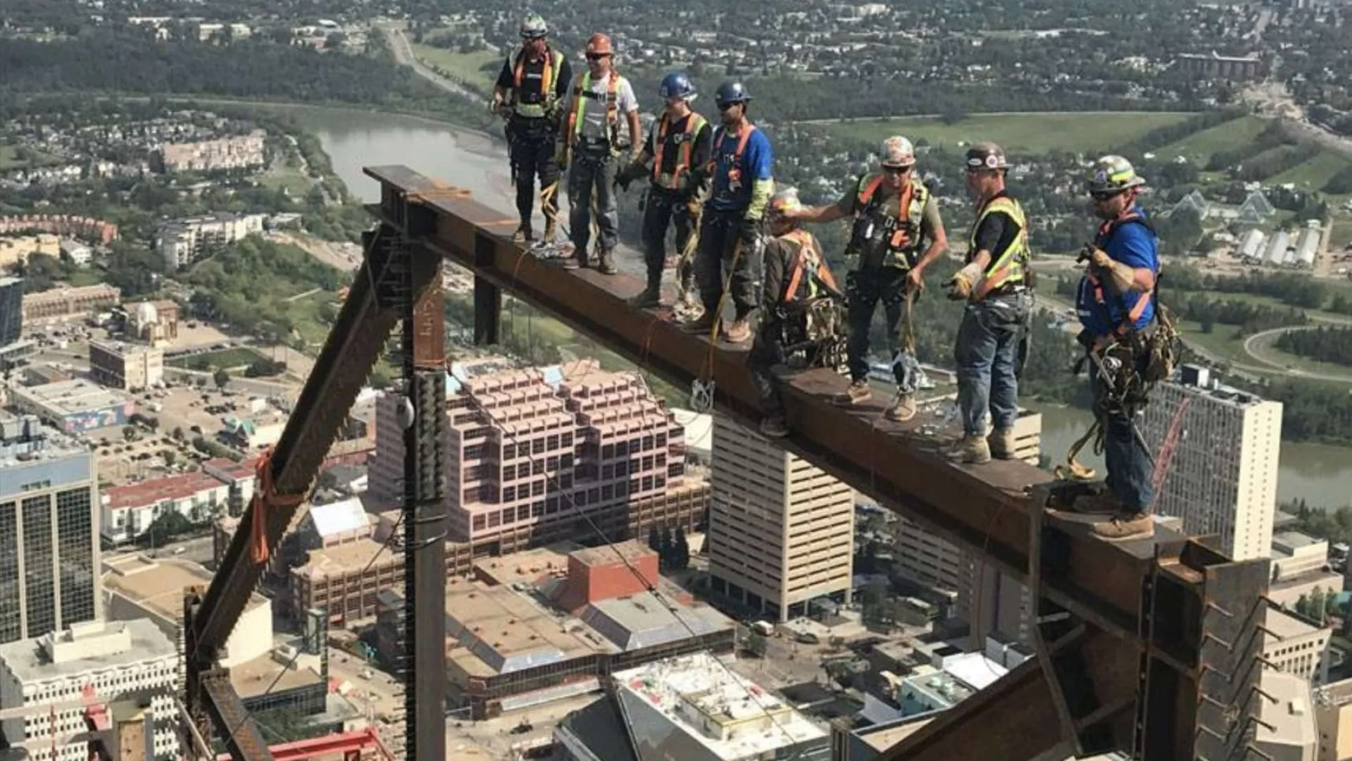 Workers in safety gear guiding heavy machinery lifting large industrial gear outdoors at construction site.