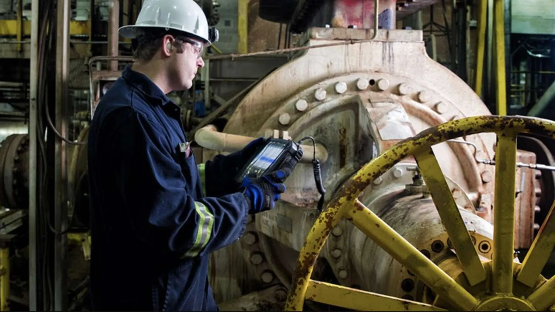 Two construction workers wearing orange helmets installing large glass panels on a building facade.