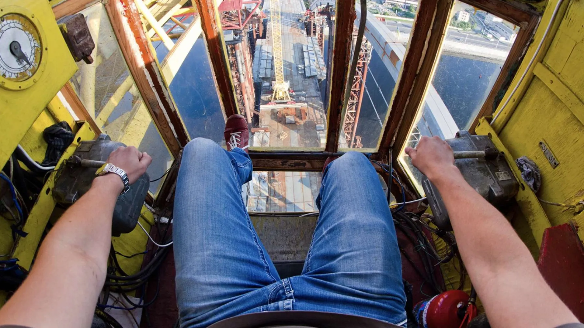 Two construction workers wearing orange helmets installing large glass panels on a building facade.
