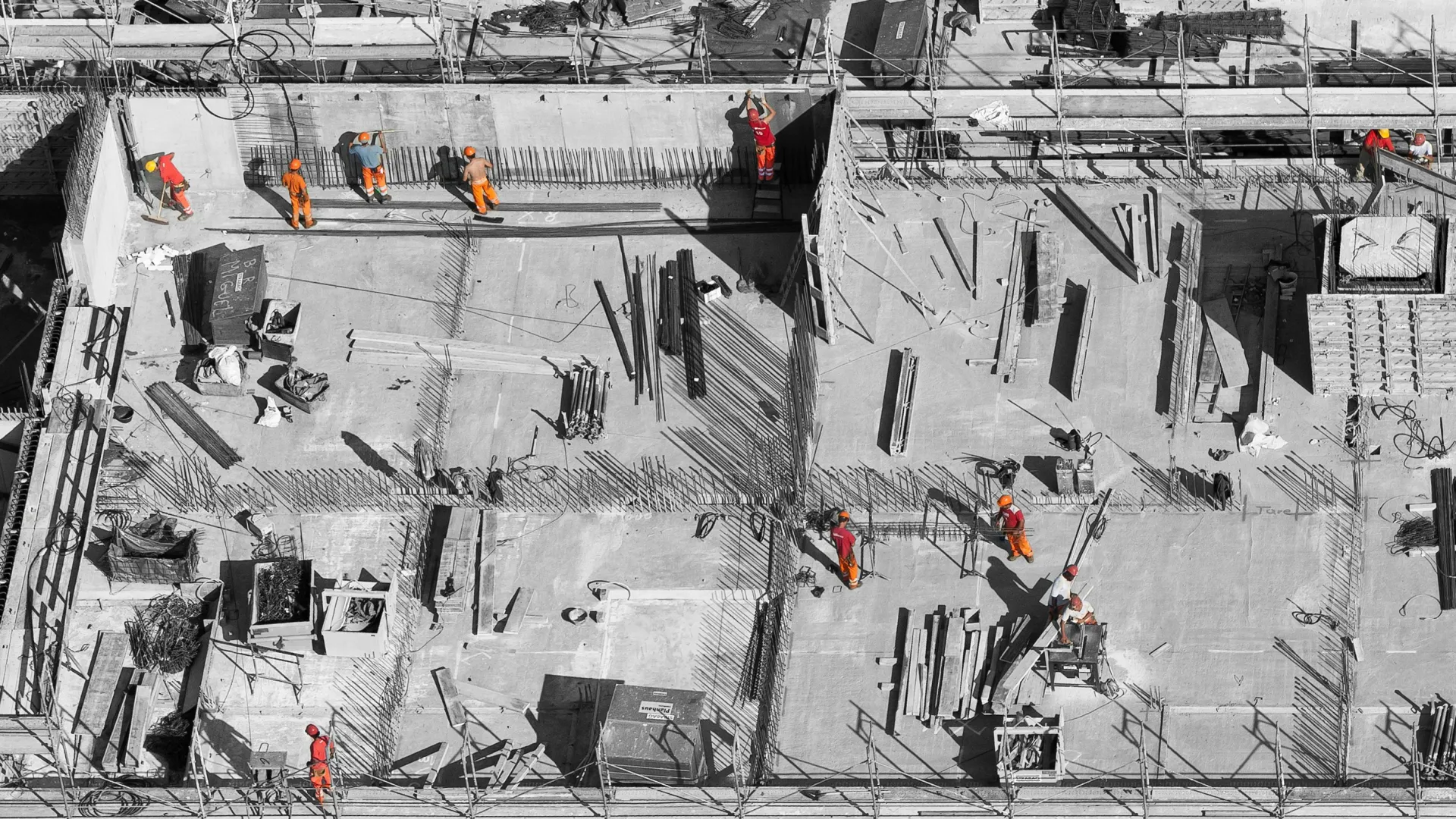 Aerial view of construction workers in safety gear on a building site, busy with structural tasks.