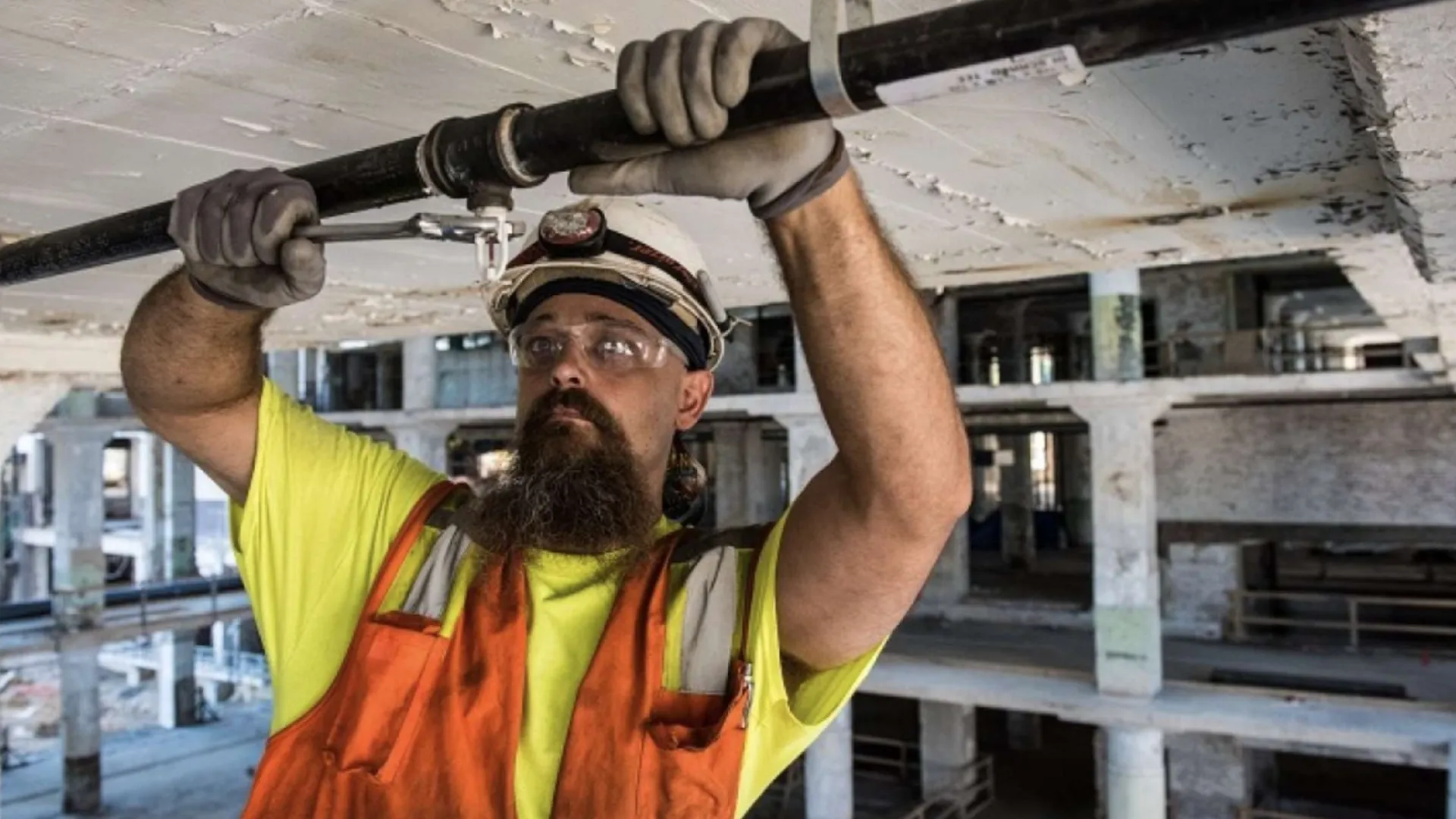 Two construction workers wearing orange helmets installing large glass panels on a building facade.