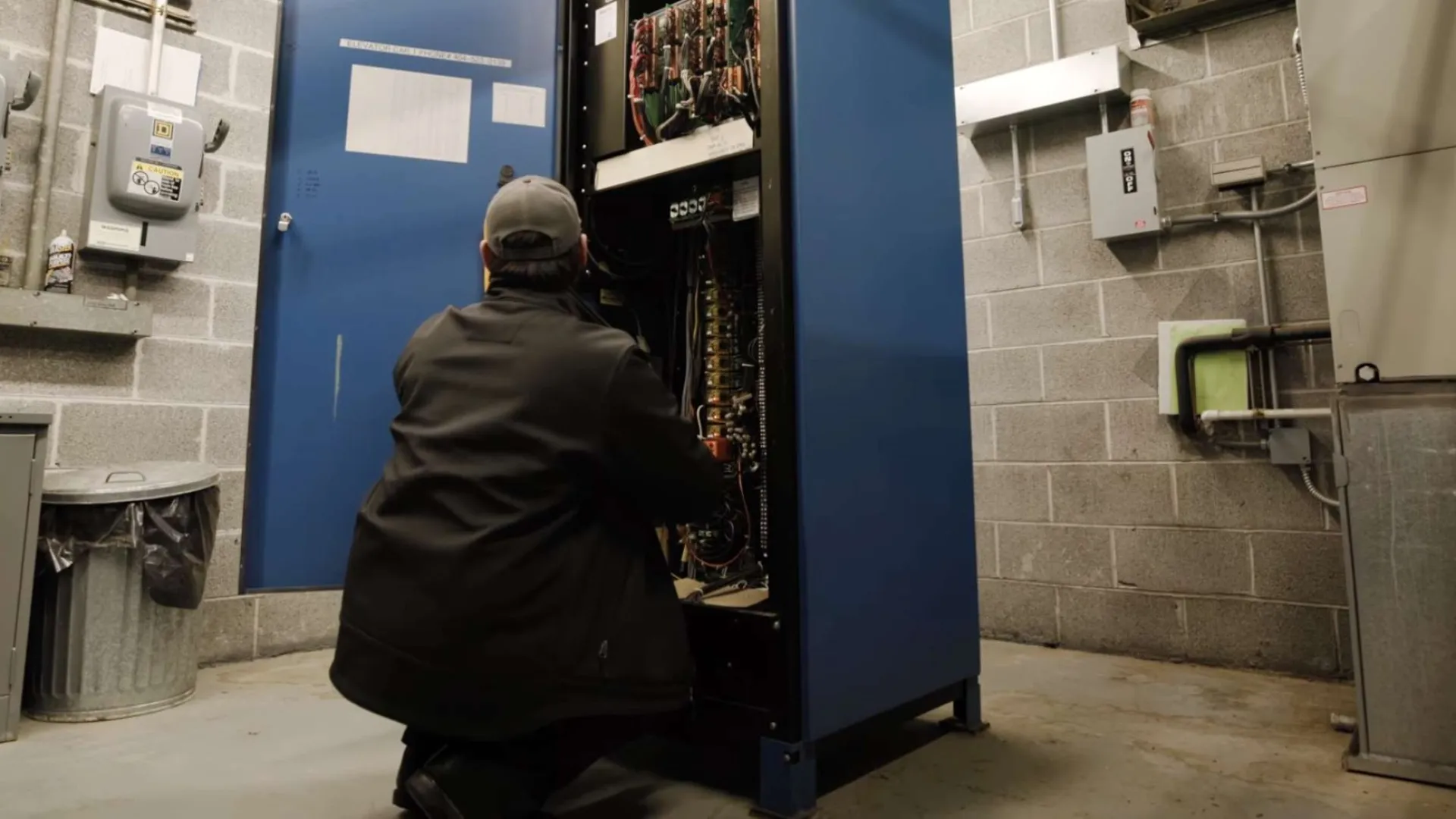 Electrician wearing yellow helmet fixing colorful wires in electrical control panel with circuit breakers.