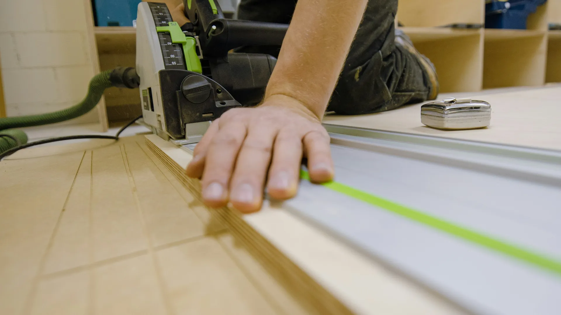 Person using a track saw to cut plywood precisely with a guide rail on a workbench indoors