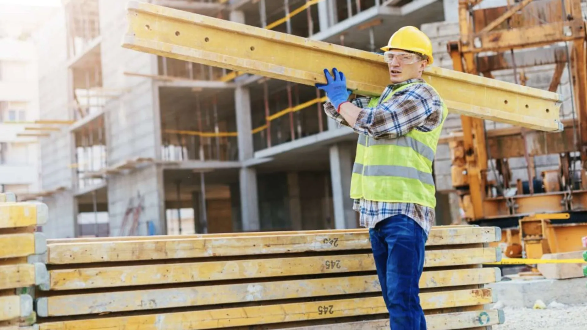 Two construction workers wearing orange helmets installing large glass panels on a building facade.