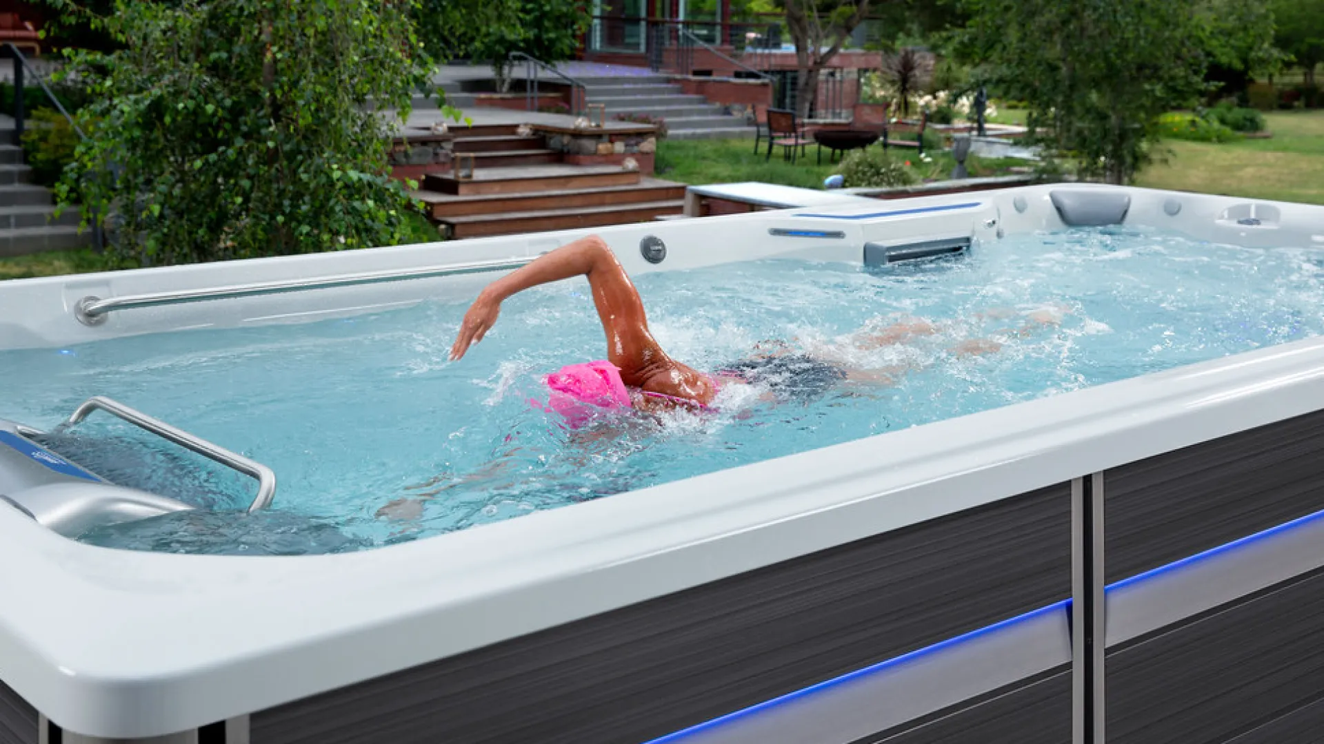 Person swimming laps in an outdoor swim spa with clear water and surrounding garden area