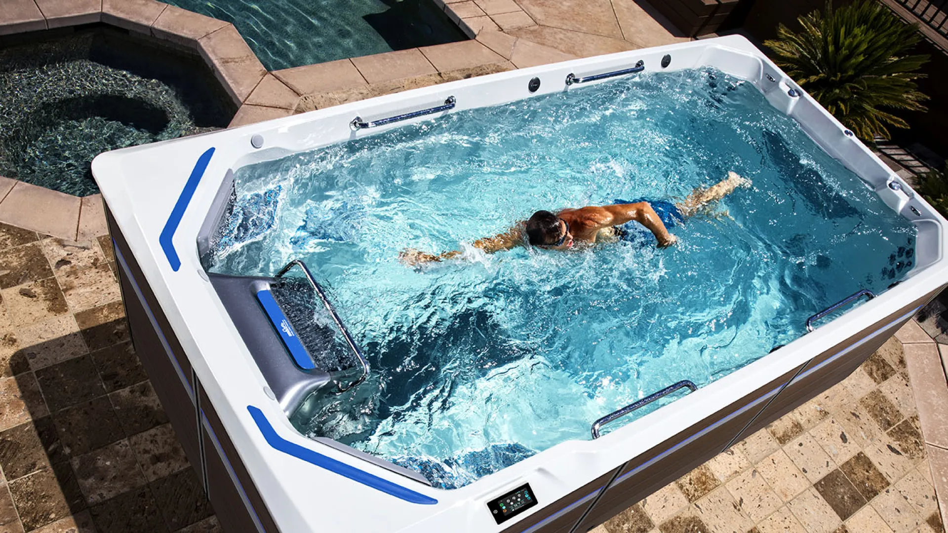 Person swimming in a large white swim spa with clear blue water in a tiled outdoor area.