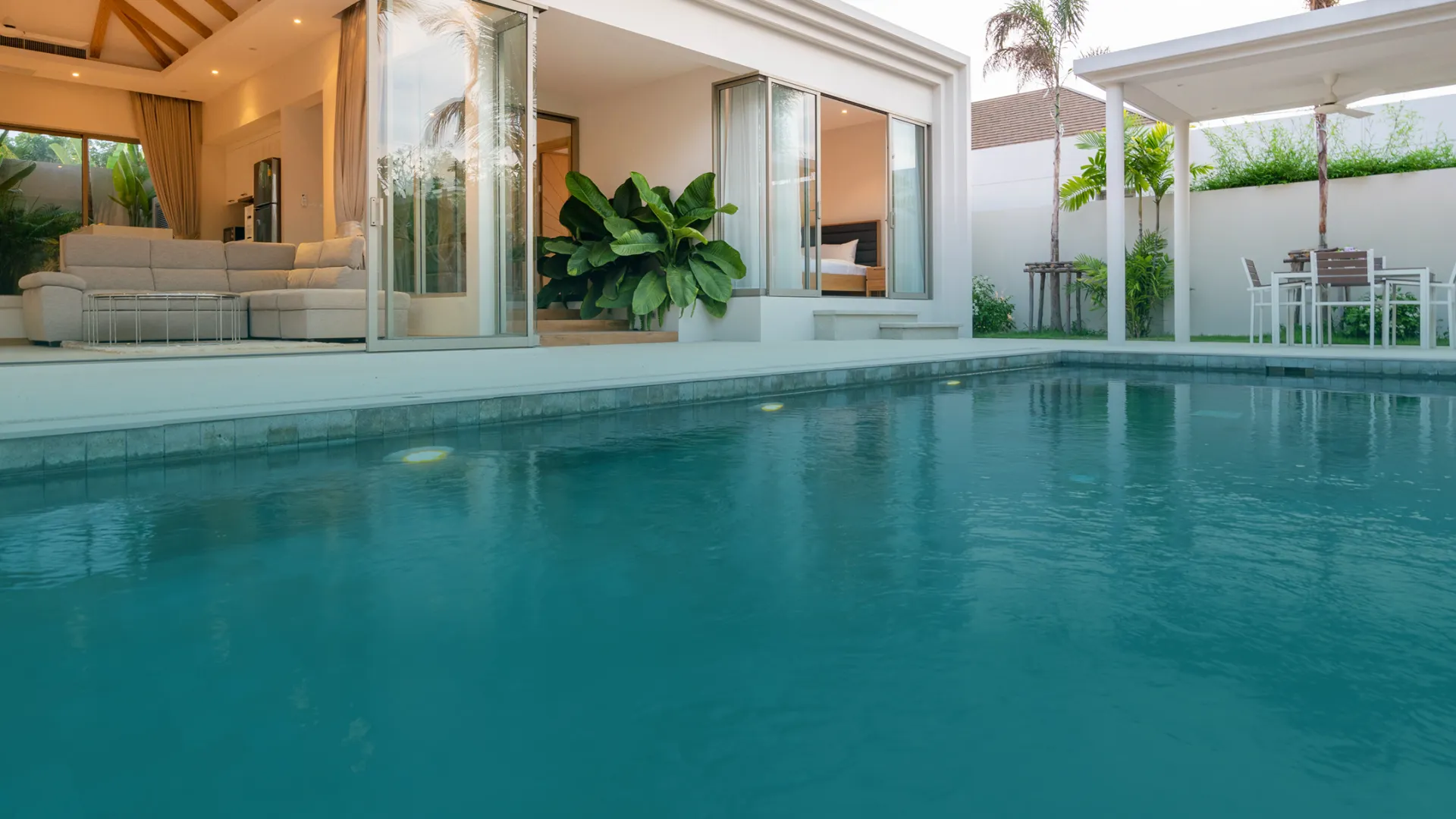 Modern home with large open living area and clear blue swimming pool under palm trees in daylight