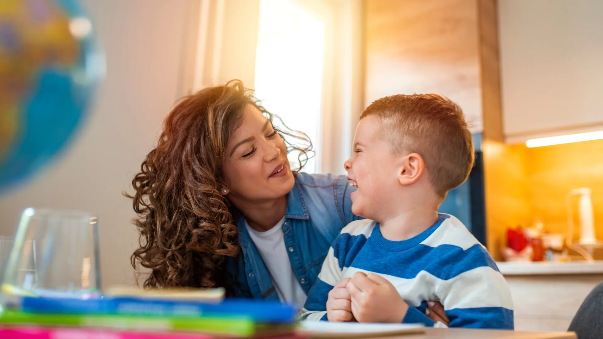 Mother and son sharing a joyful moment while sitting at a table with books in a bright home setting