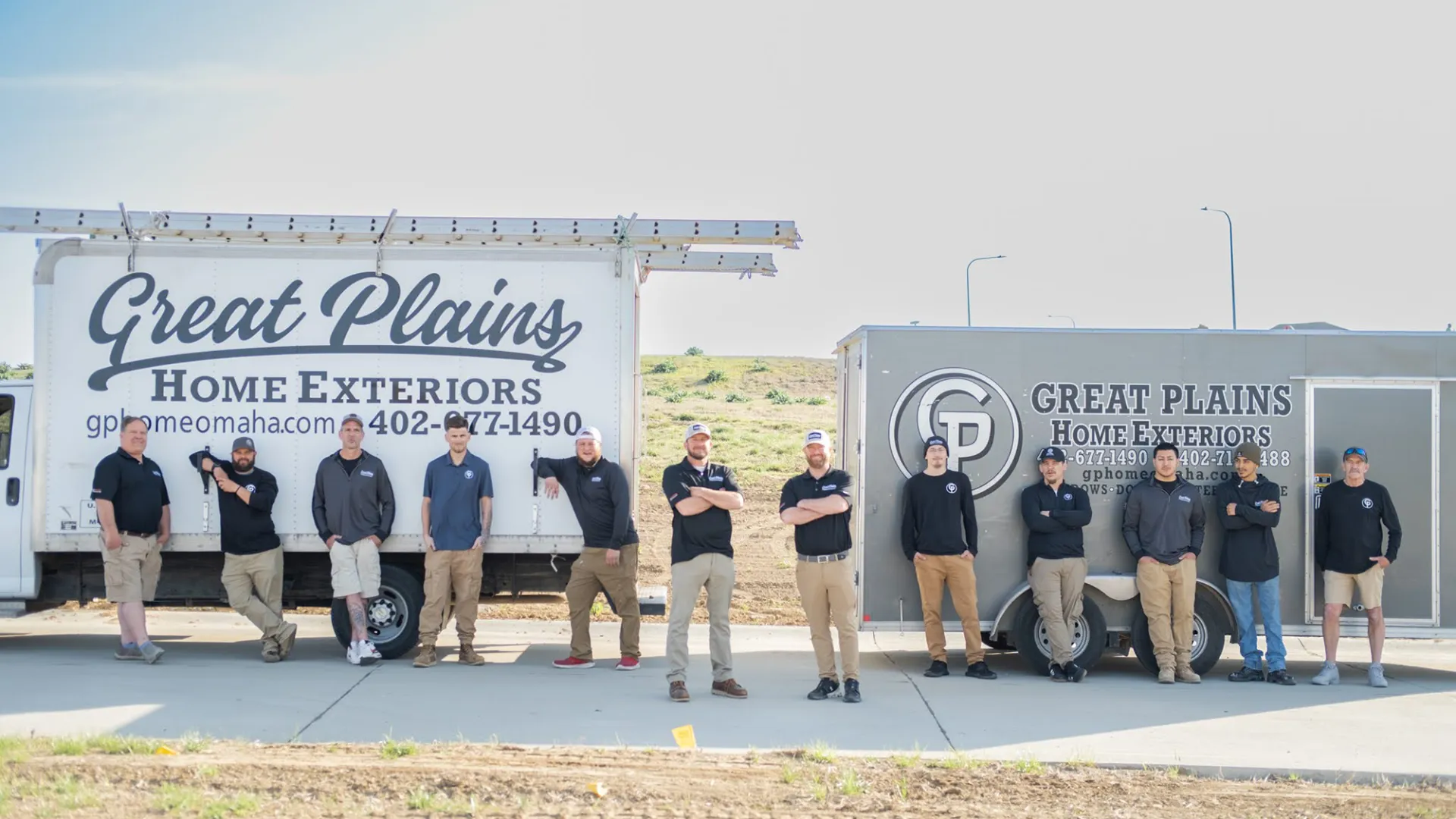 Team members of Great Plains Home Exteriors stand between company trucks on a sunny day outside.