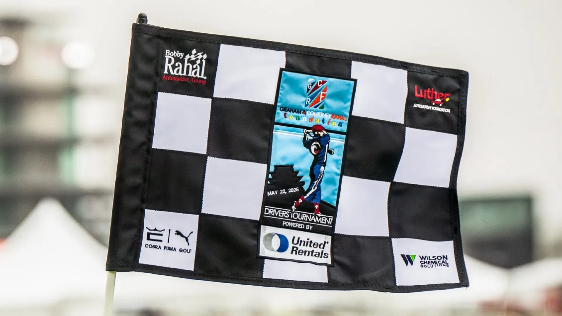 Black and white checkered flag with event and sponsor logos for the Granville Charity Drivers Tournament May 22, 2025
