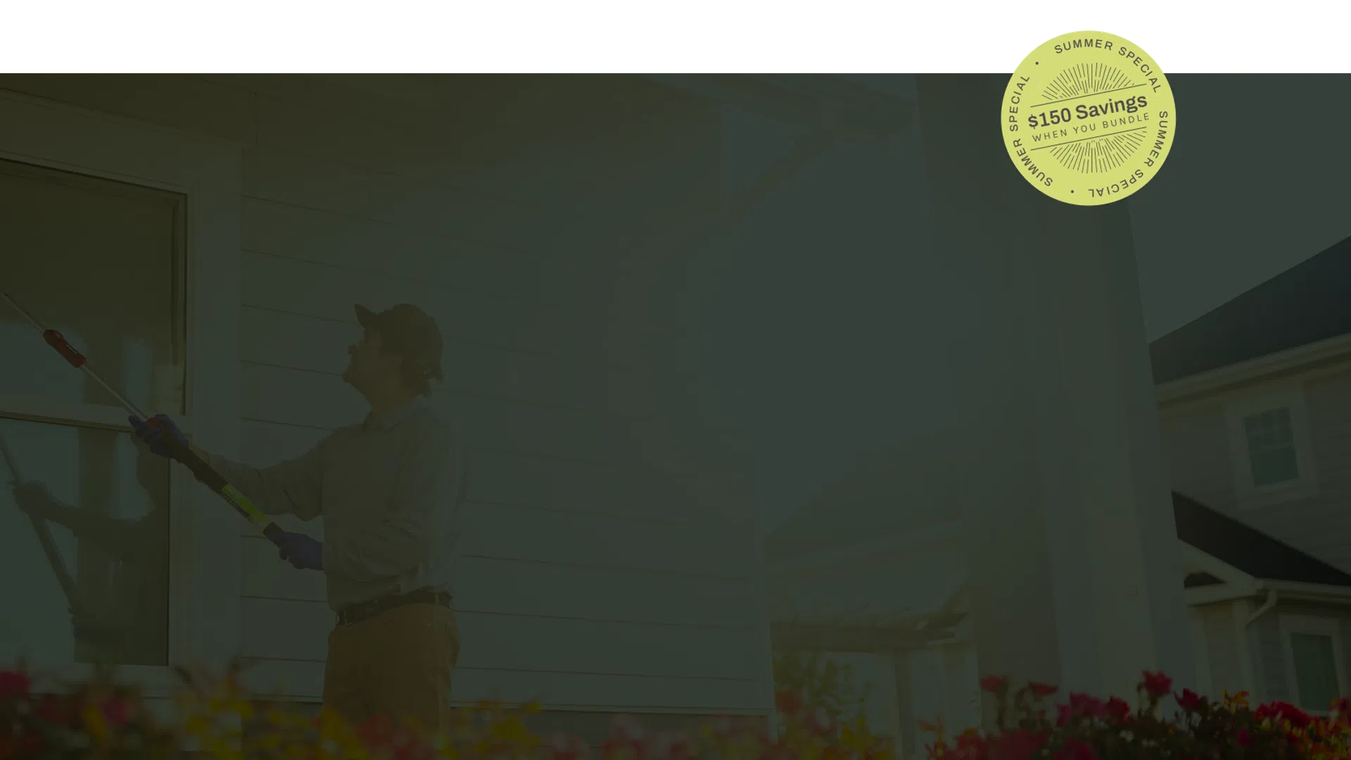 Man cleaning exterior house window with a long duster during daytime near flowers in front yard.