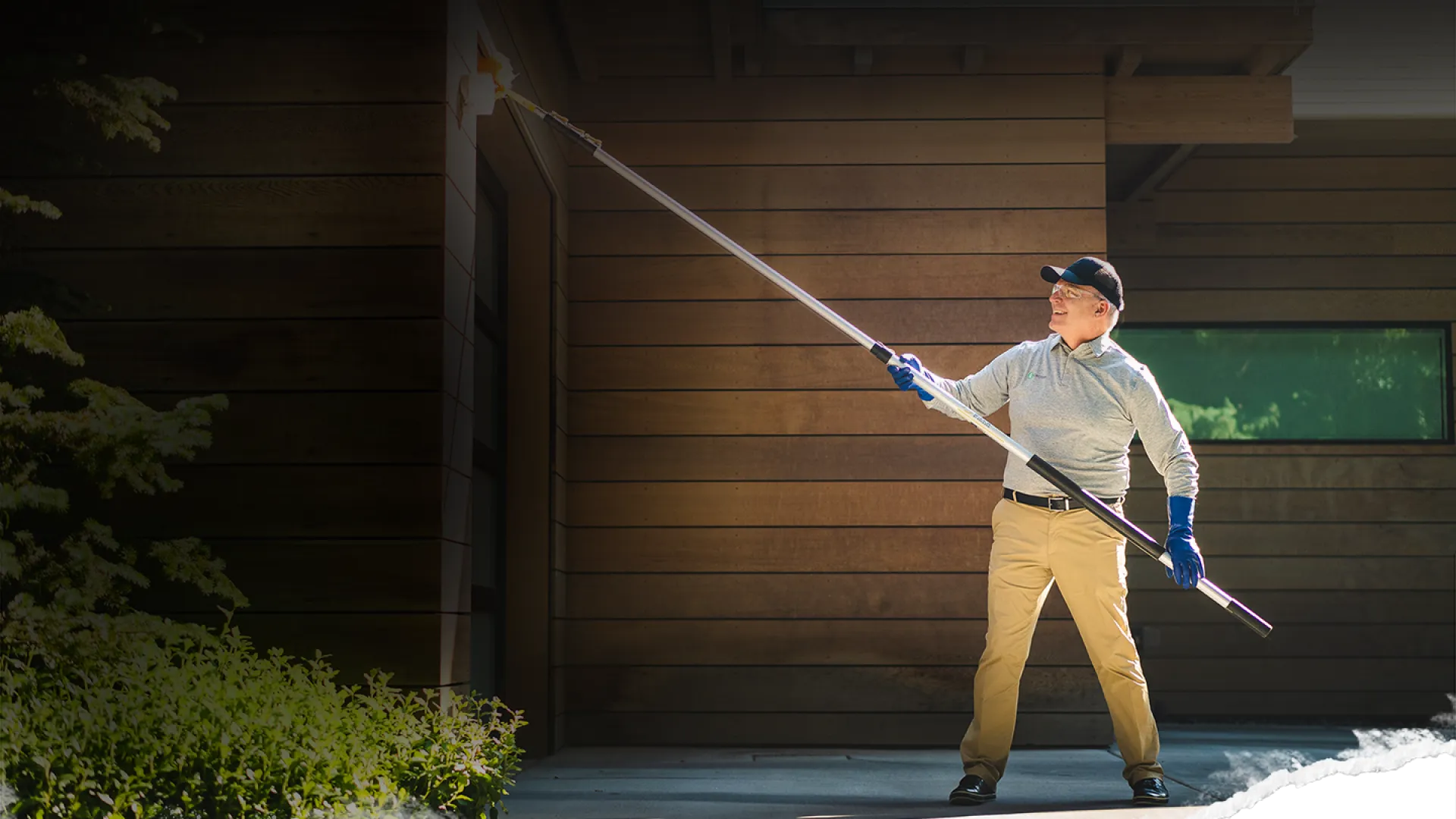 Pest control service technician servicing a customers home with an eave sweep brush.