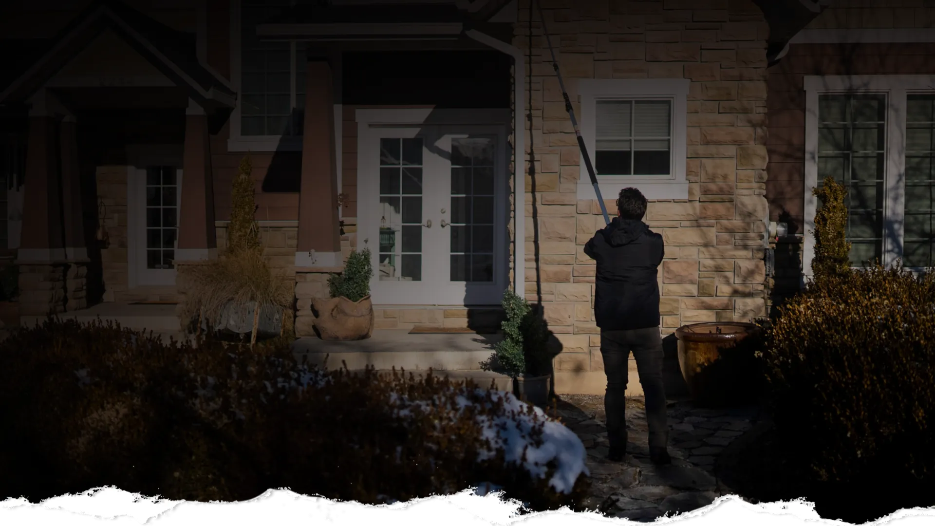 Person cleaning house exterior windows with a long pole washer on a sunny day.