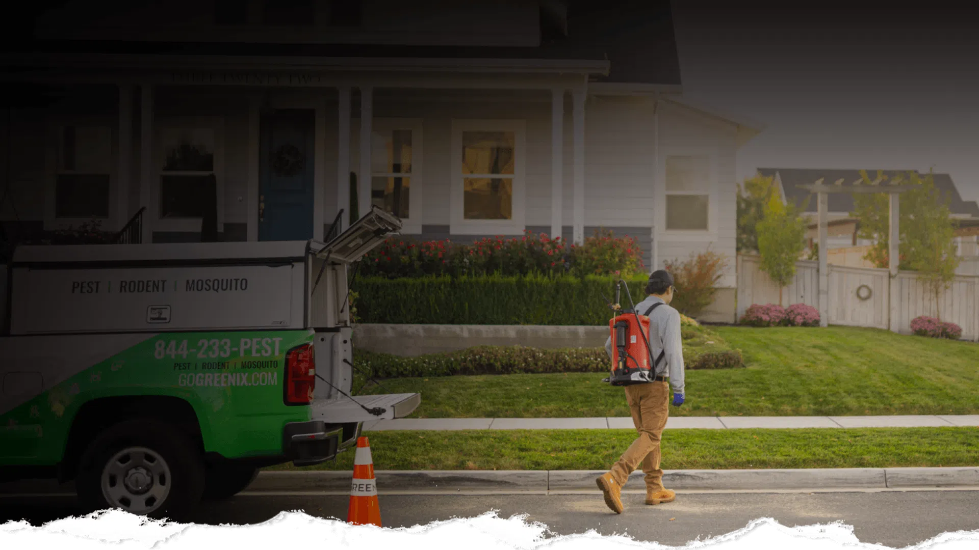 Pest control worker in protective gear walking near a green and white truck outside a suburban house.