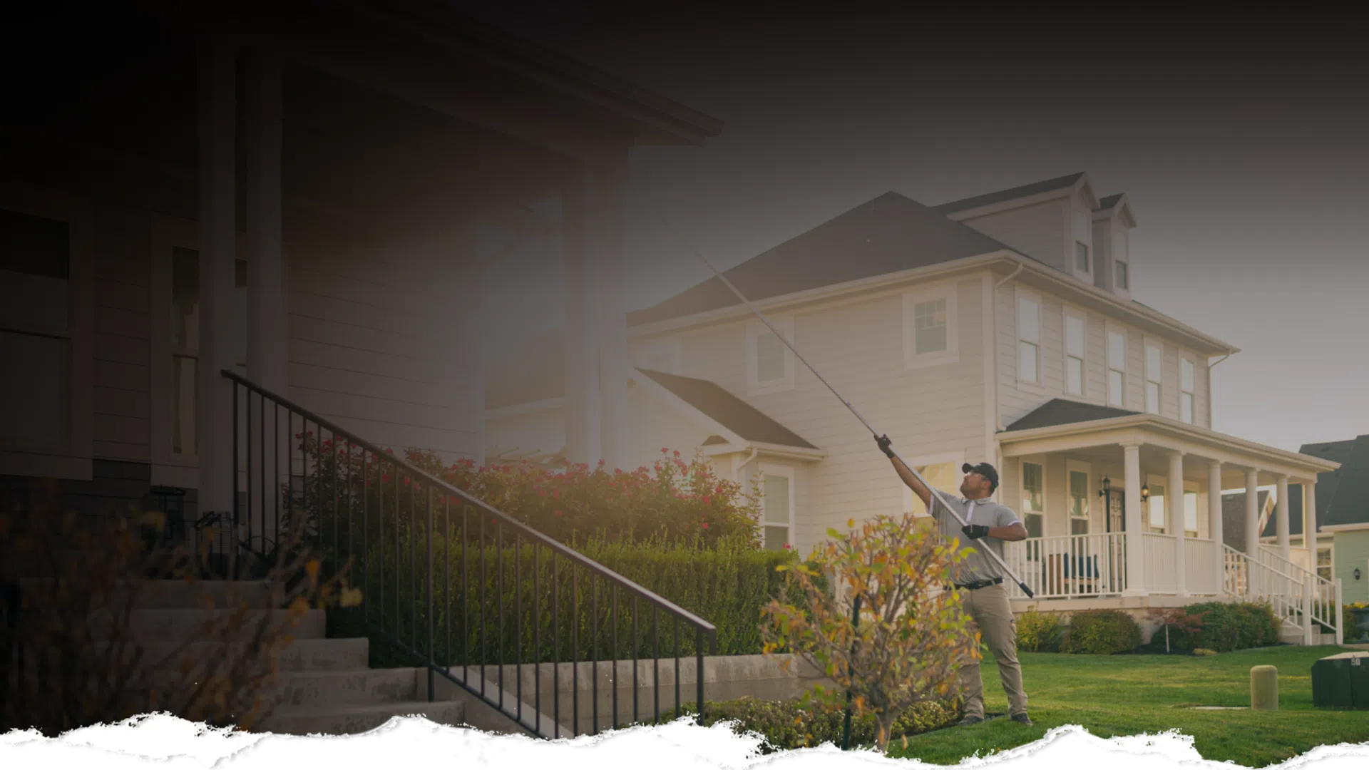 Man treating pests on house windows with a long pole outside a suburban two-story home during daytime